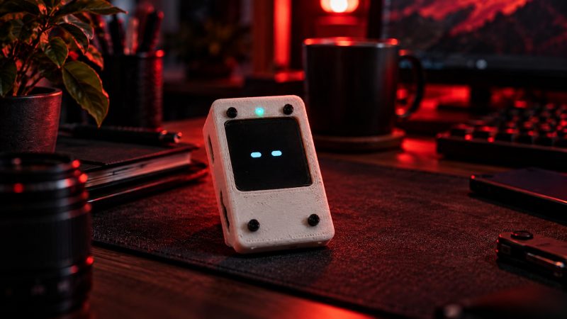 A small black handheld device with a blank screen resting on a desk in red light