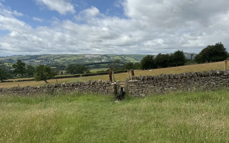 A dry stone wall and a black dog by a stile, with the Peak District hills beyond