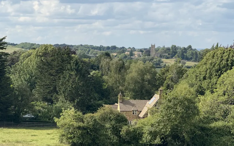 Cotswold countryside with a church tower on the horizon and a stone cottage tucked among the trees